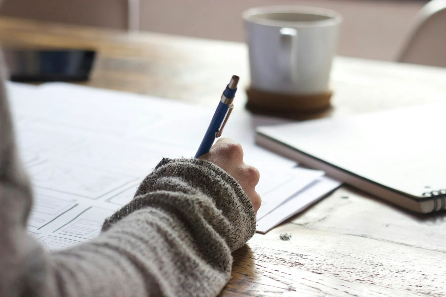 A person writing notes in a notebook beside a cup of coffee